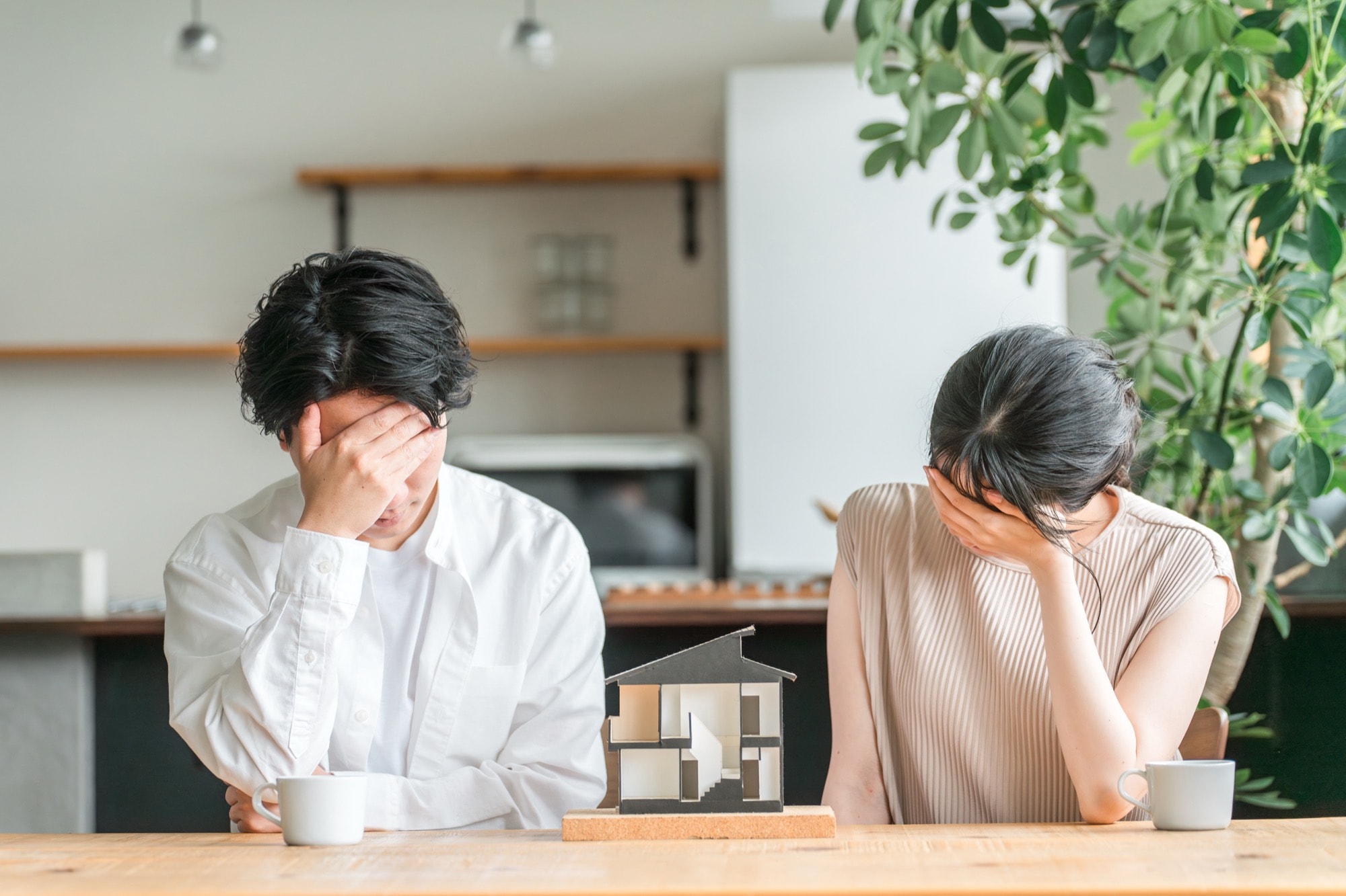 家の模型の前で頭を抱える夫婦